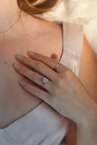 Close-up of a hand wearing a gold ring with a diamond on a light background