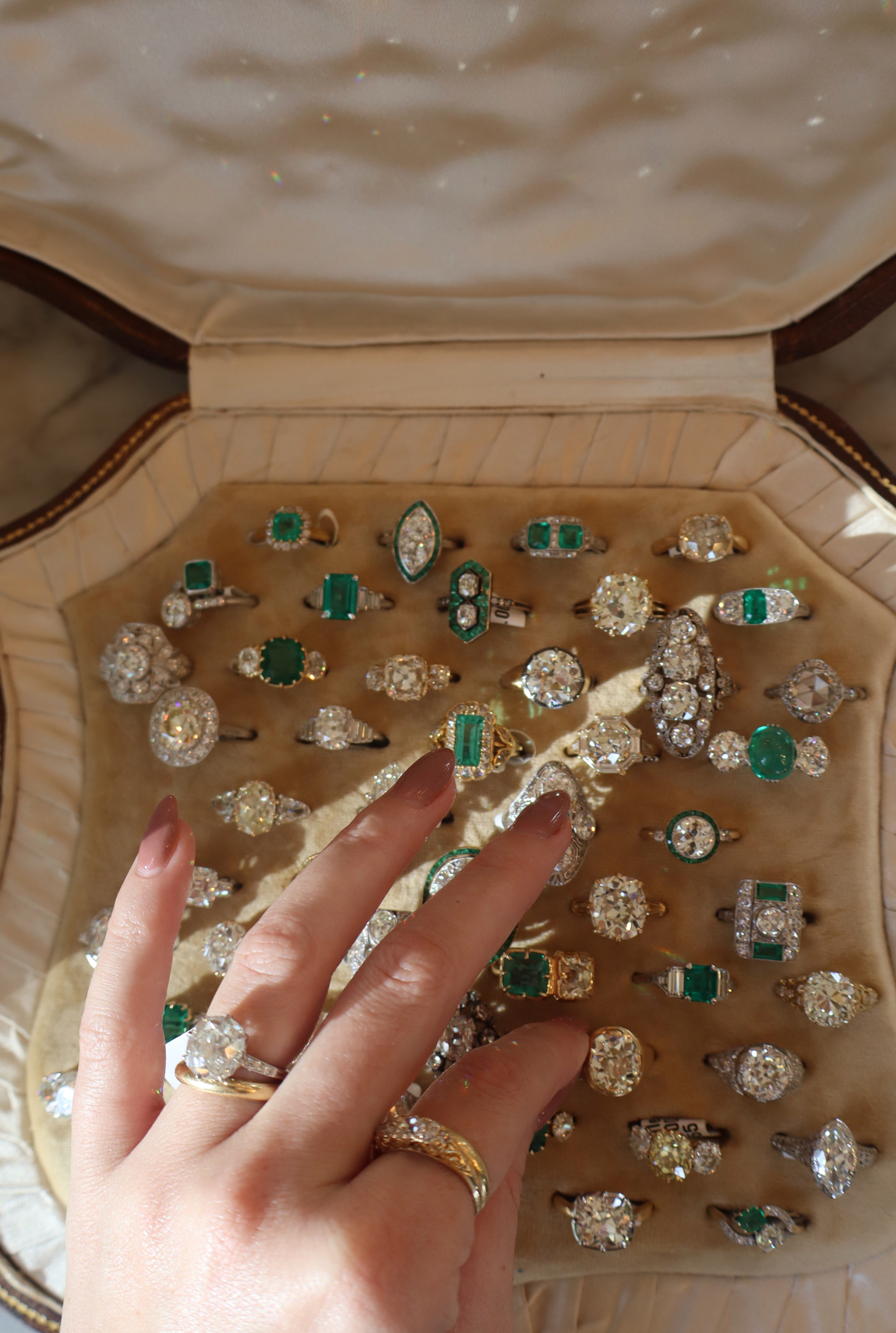 Collection of rings with green gemstones displayed in an open jewelry box, with a hand wearing a gold ring for scale.